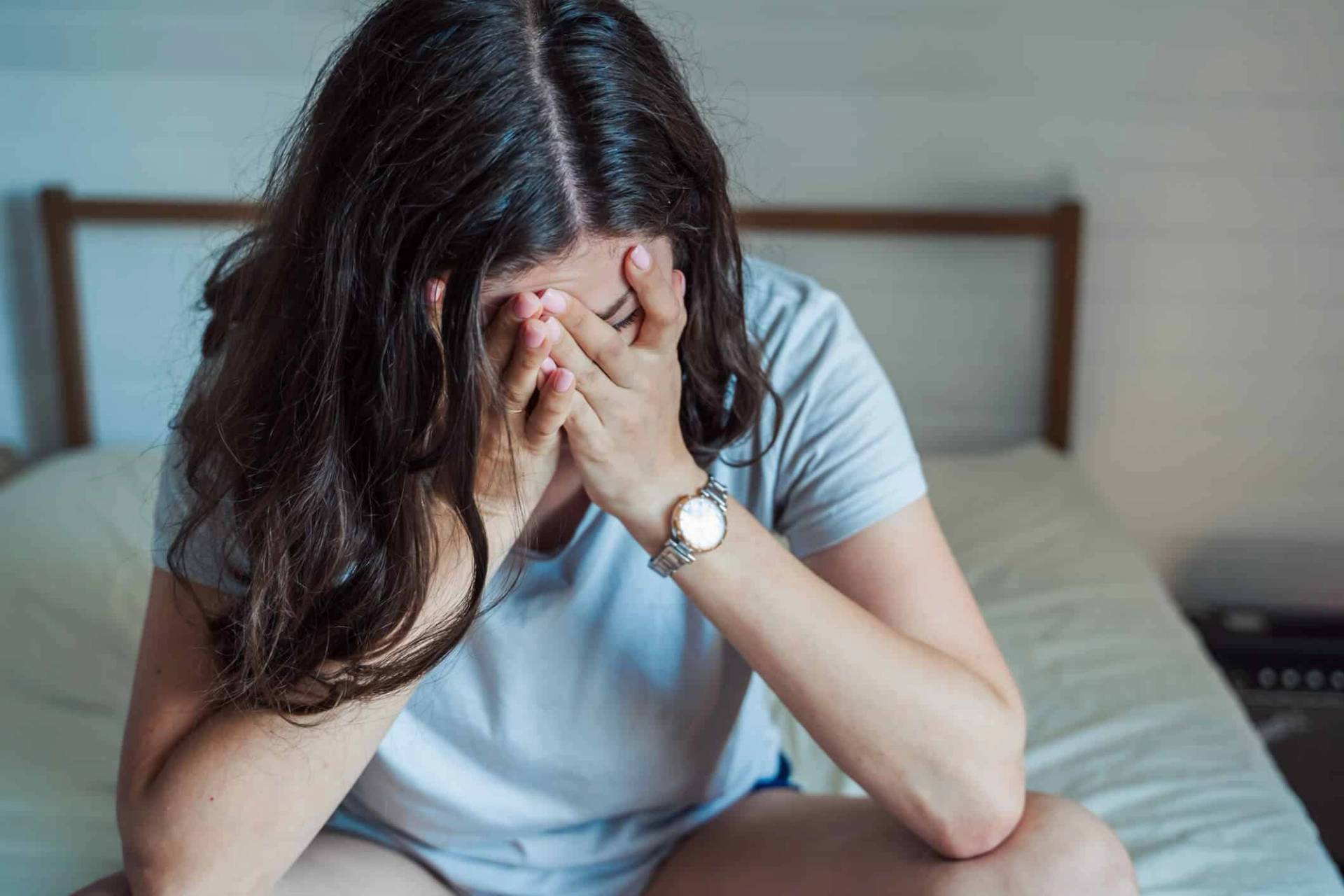 Femme assise sur un lit, le visage caché dans les mains.