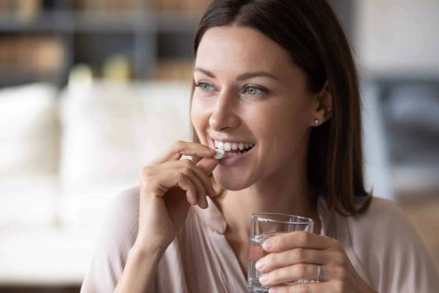 Femme prenant un comprimé avec un verre d’eau.