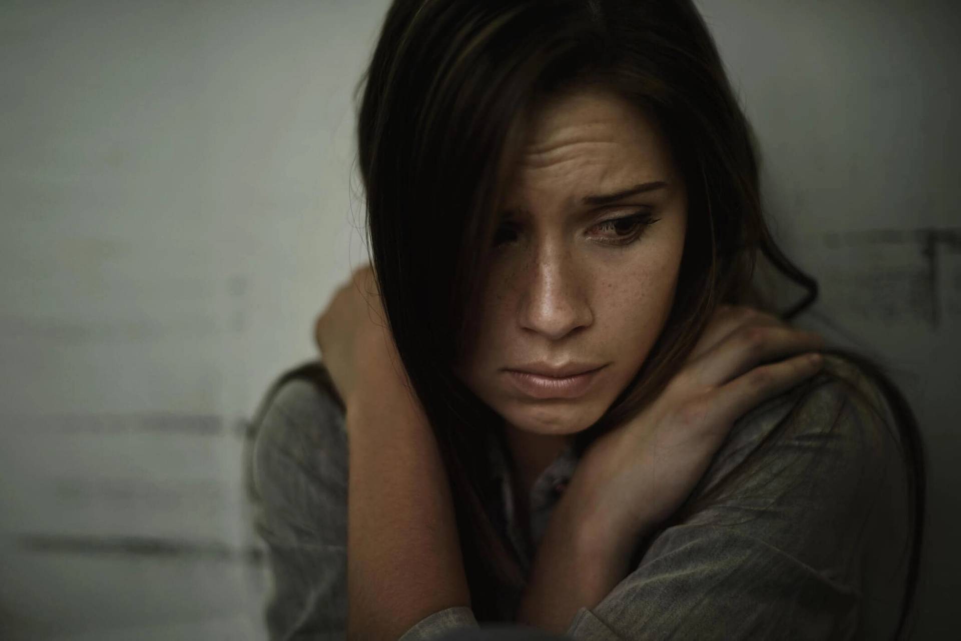 Femme repliée sur elle-même, une main sur l’épaule.
