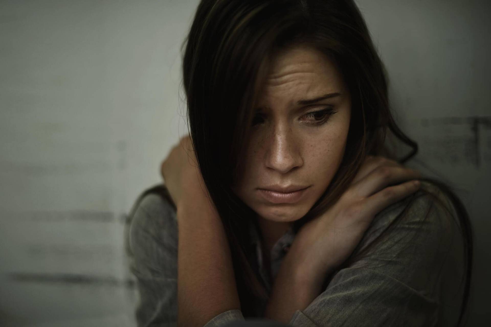 Femme repliée sur elle-même, une main sur l’épaule.