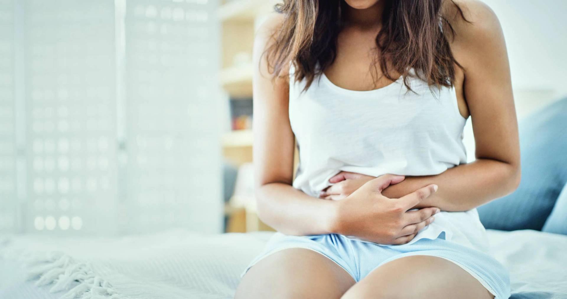 Jeune femme souffrant de douleurs abdominales ou de gastro-entérite, assise sur un lit.
