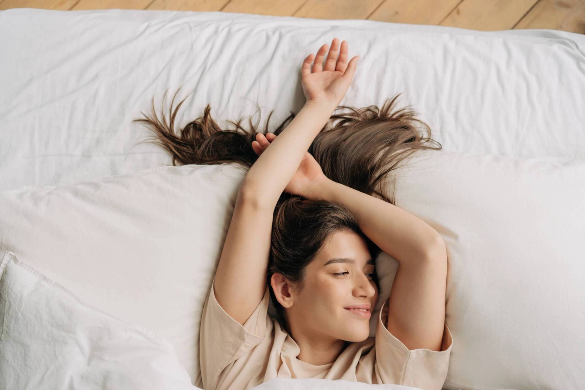 Femme allongée sur un lit, les bras au-dessus de la tête.