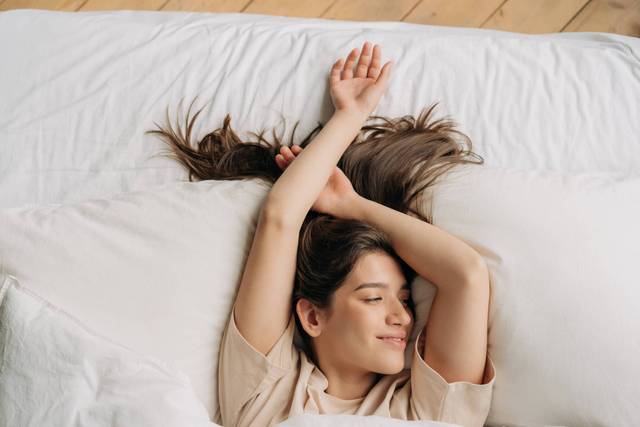 Femme allongée sur un lit, les bras au-dessus de la tête.