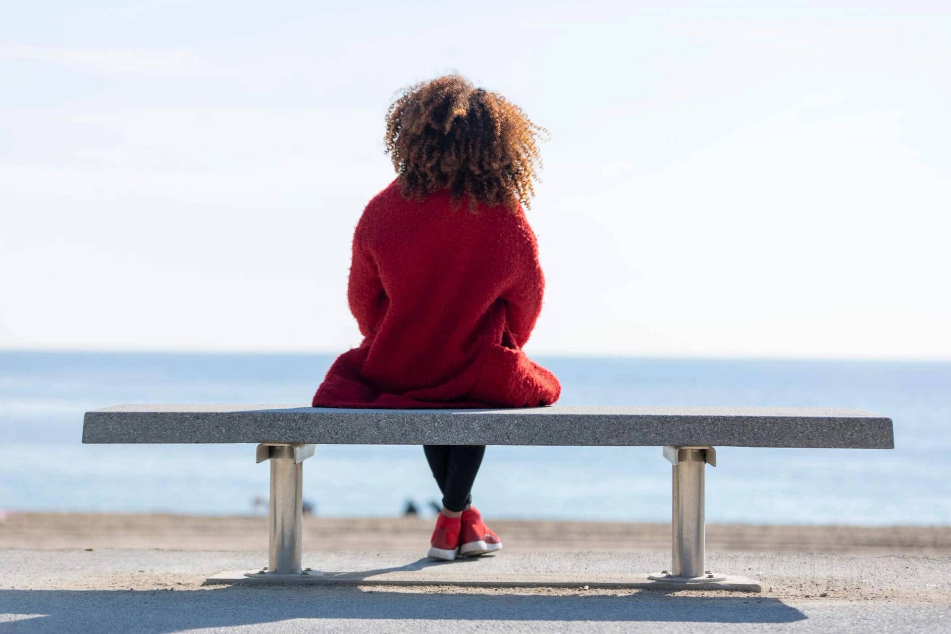 Femme assise sur un banc face à la mer.