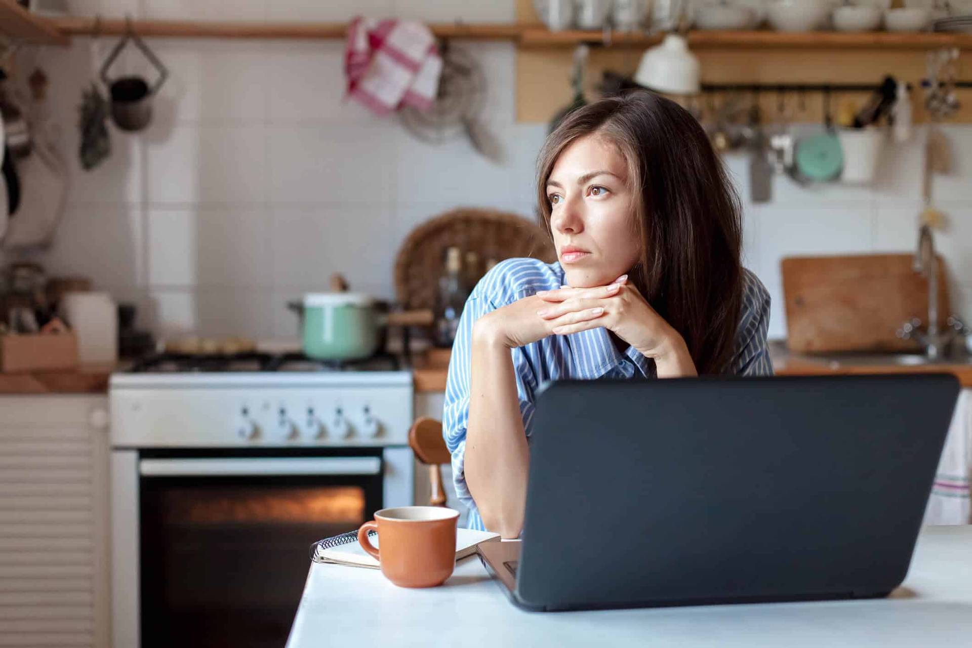 Femme devant un ordinateur à la maison, regardant à l’écart.