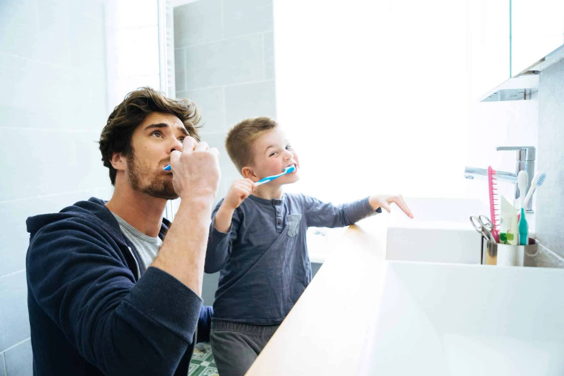 Adulte et enfant se brossant les dents devant un miroir.
