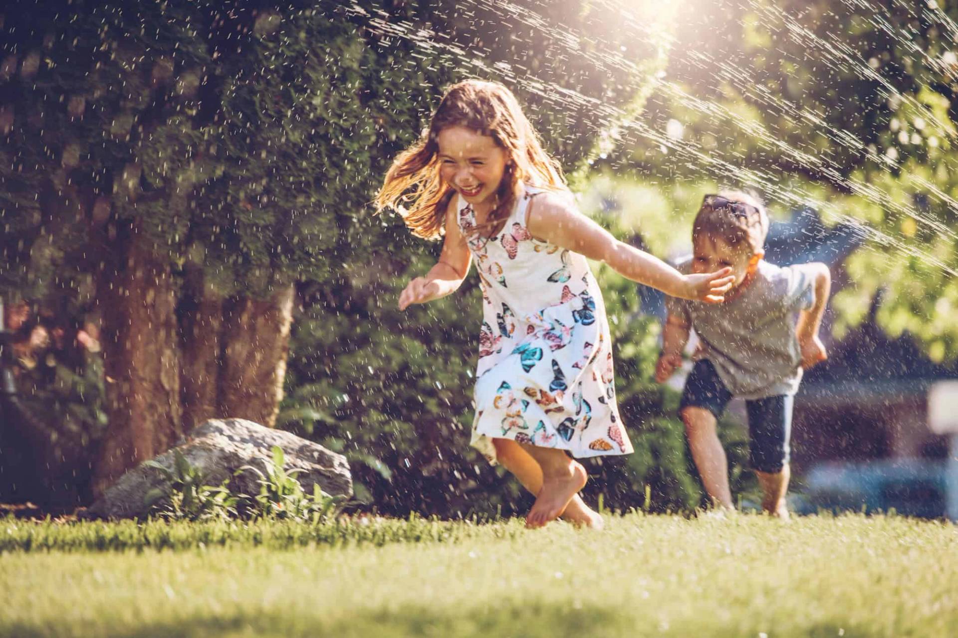 Deux enfants courant dans un jardin arrosé.