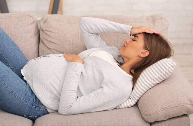 Femme au ventre arrondi allongée avec une main sur le front.