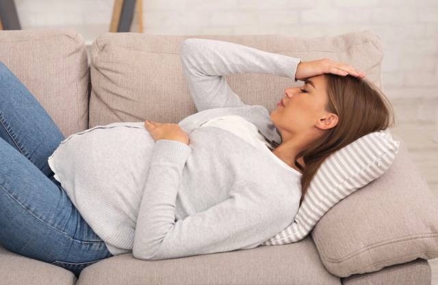 Femme au ventre arrondi allongée avec une main sur le front.