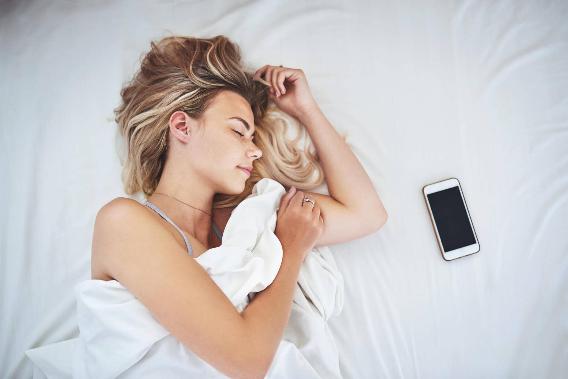 Femme endormie dans un lit, un téléphone près d’elle.