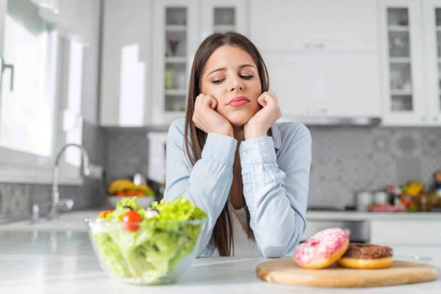 Femme devant un saladier et des pâtisseries, le menton posé dans ses mains.