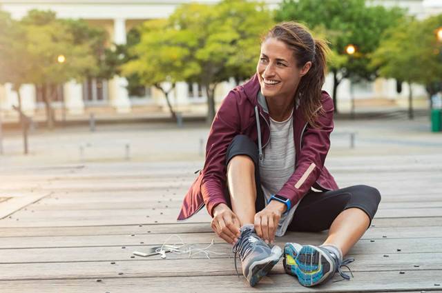 Femme en tenue de sport nouant ses chaussures à l’extérieur.