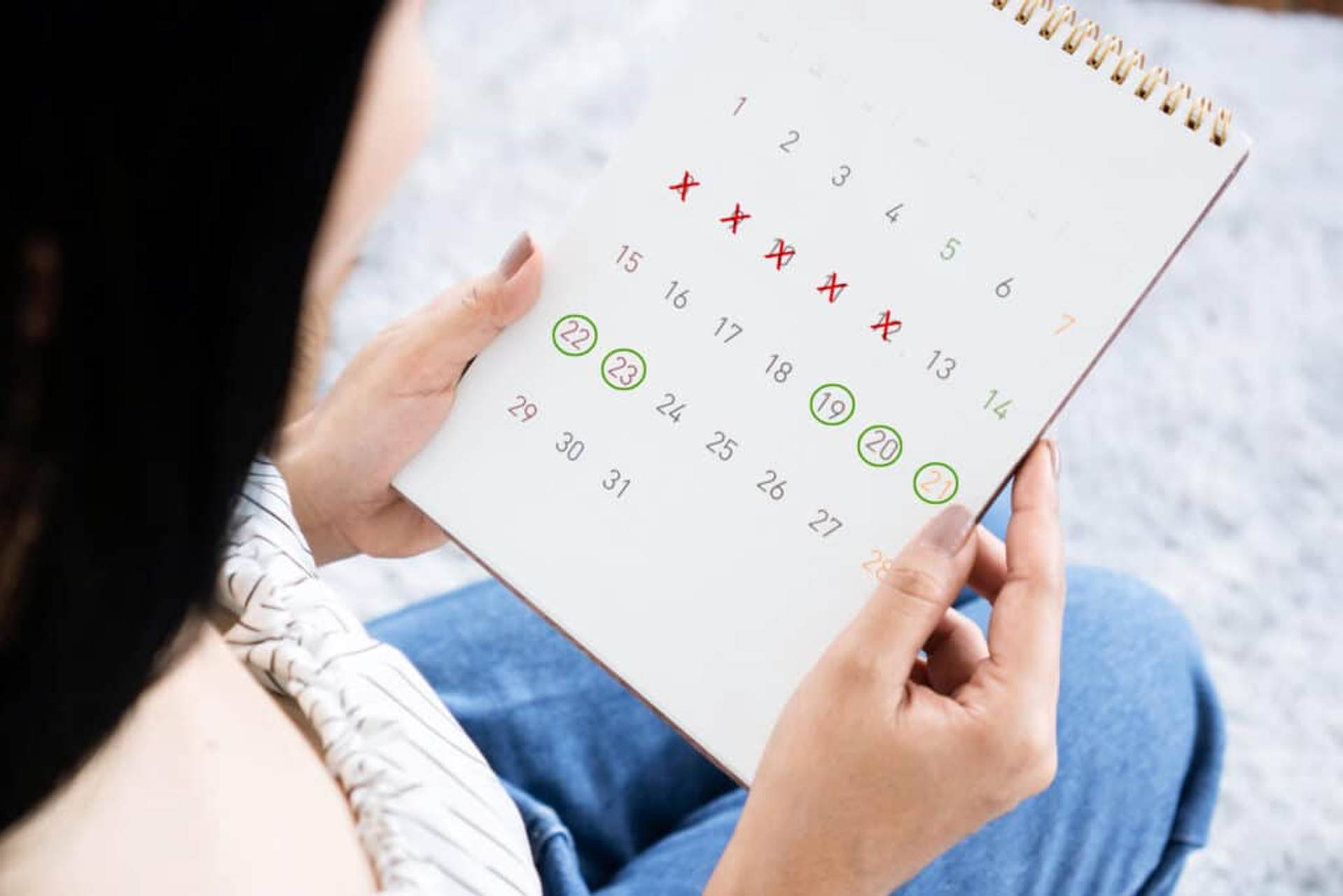 Personne tenant un calendrier comportant des dates entourées et barrées.