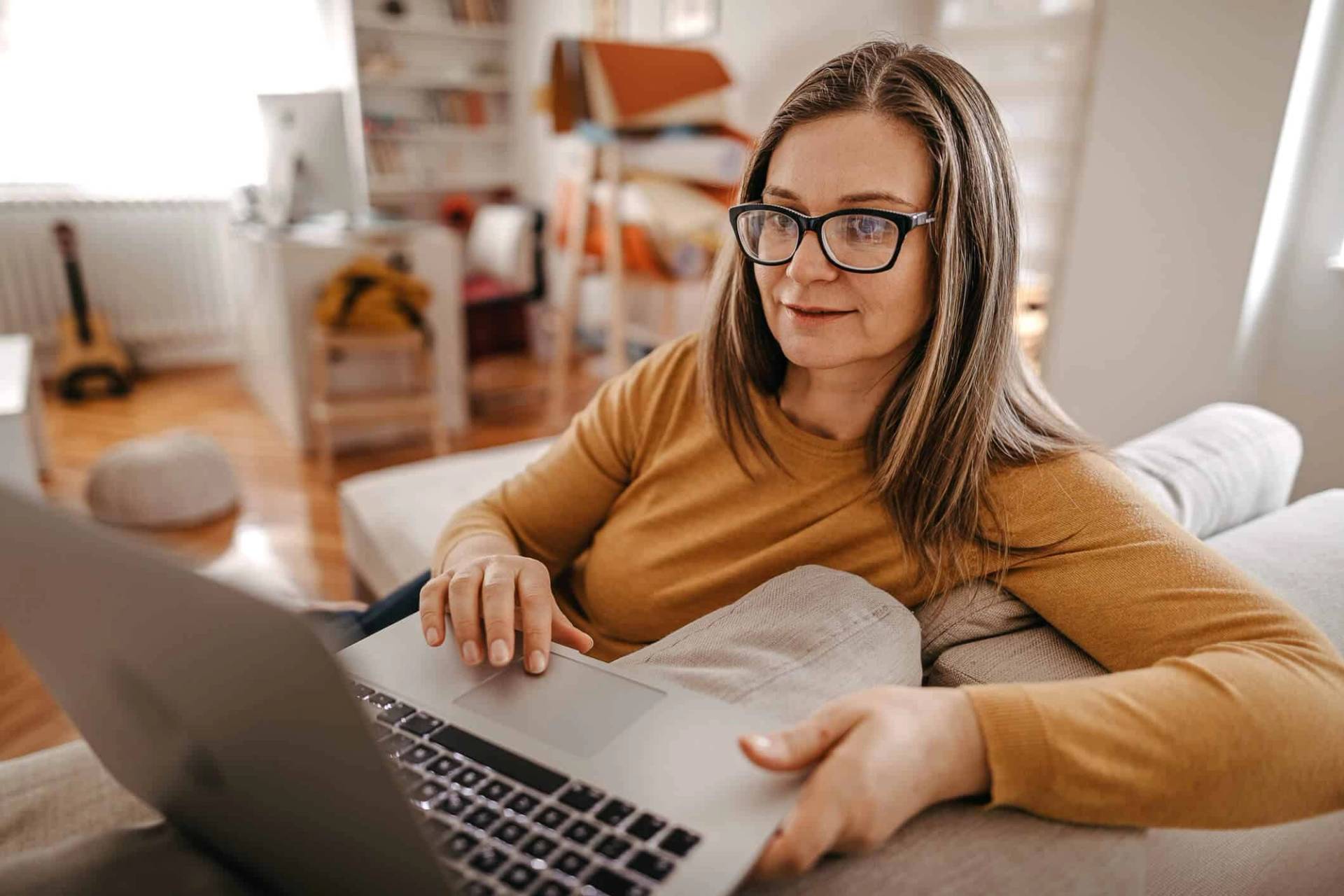 Femme installée sur un canapé, regardant un ordinateur portable.