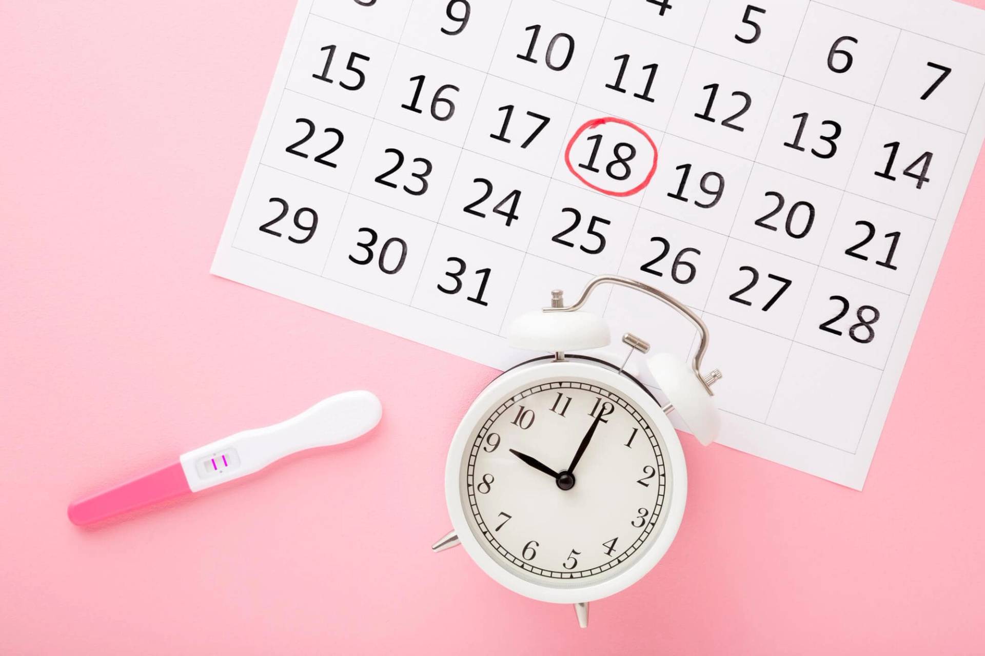 Calendrier, réveil et test sur un fond rose.