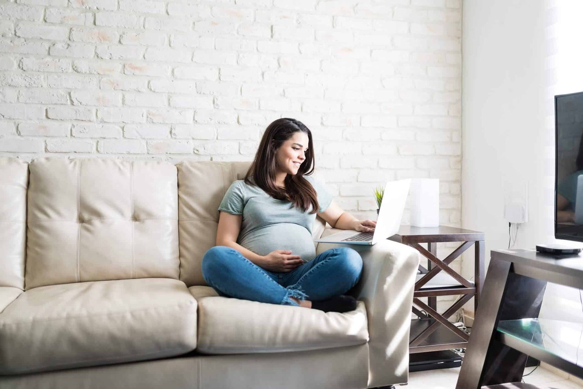 Femme au ventre arrondi utilisant un ordinateur sur un canapé.