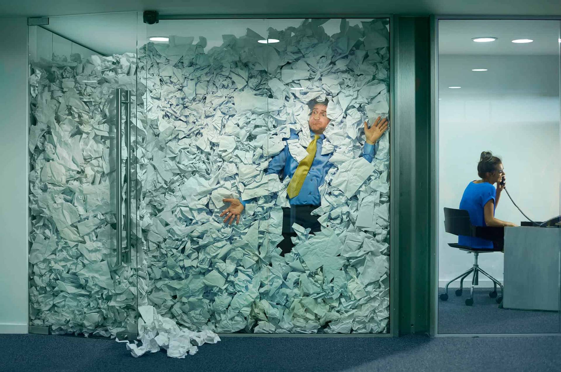 Montage représentant un homme submergé de papiers dans un bureau vitré.