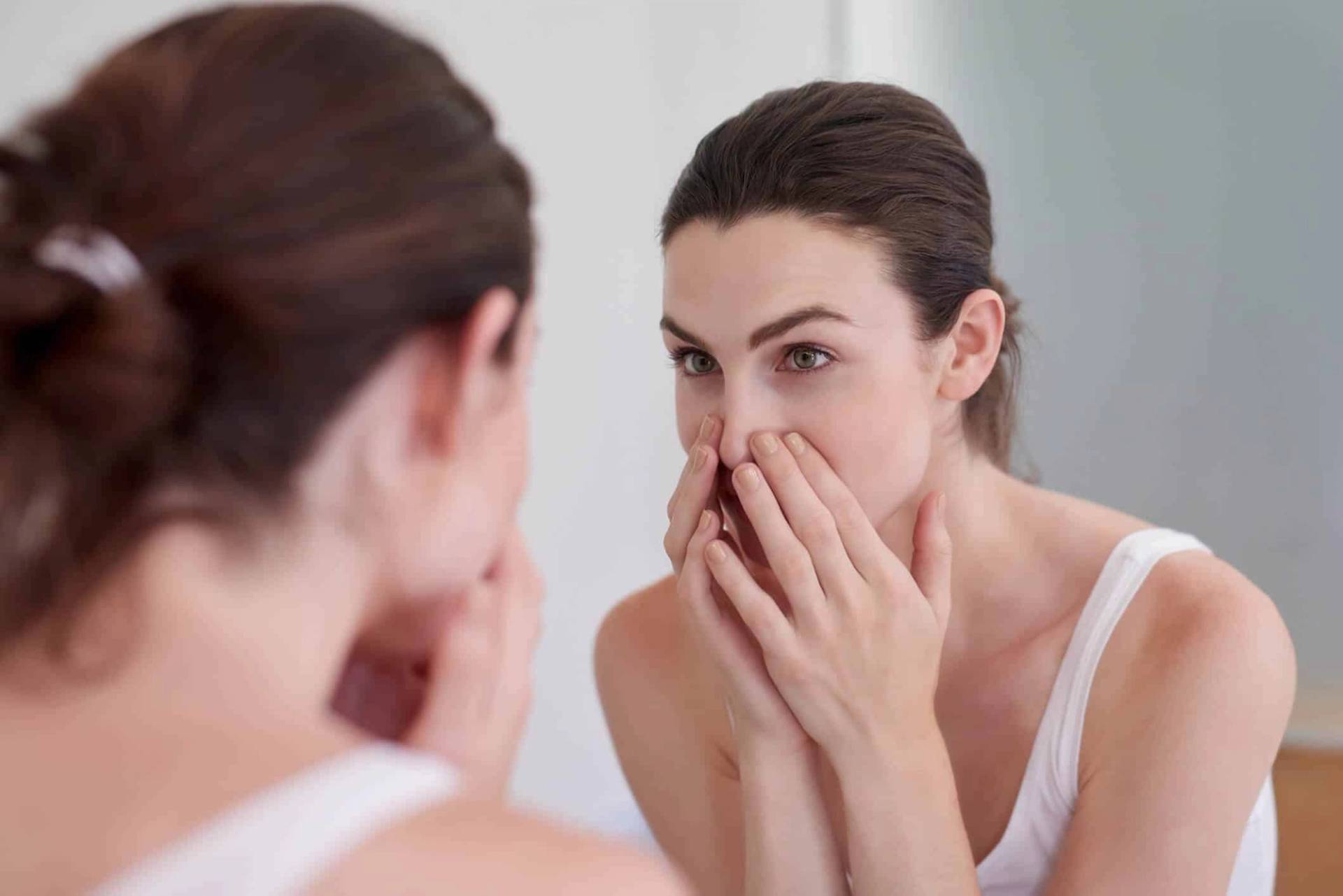 Femme examinant son nez devant un miroir.