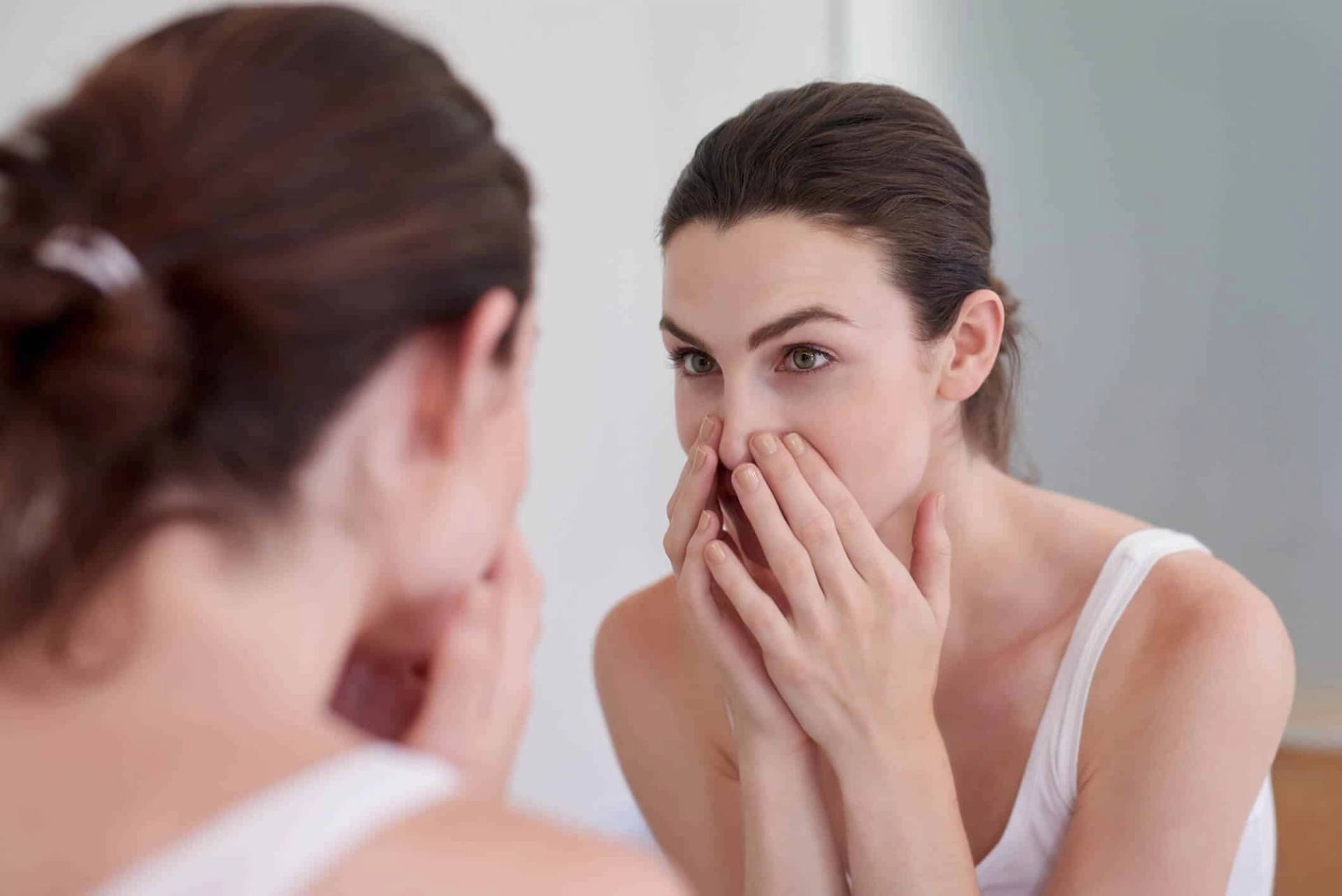 Femme examinant son nez devant un miroir.