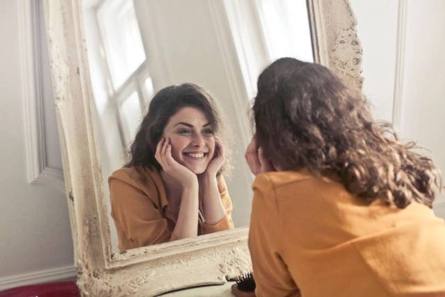 Une femme joyeuse sourit à son reflet dans un miroir de style vintage, dégageant positivité et chaleur