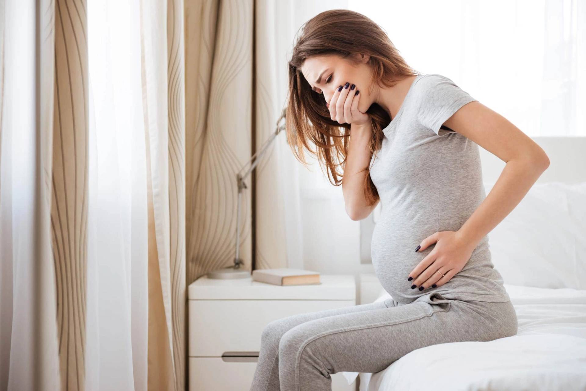 Femme au ventre arrondi tenant sa bouche et son ventre.