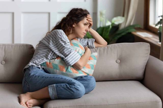 Femme au ventre arrondi assise sur un canapé avec un coussin.
