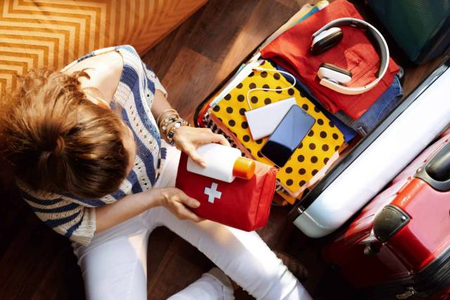 Personne préparant une trousse de premiers secours près d’une valise.