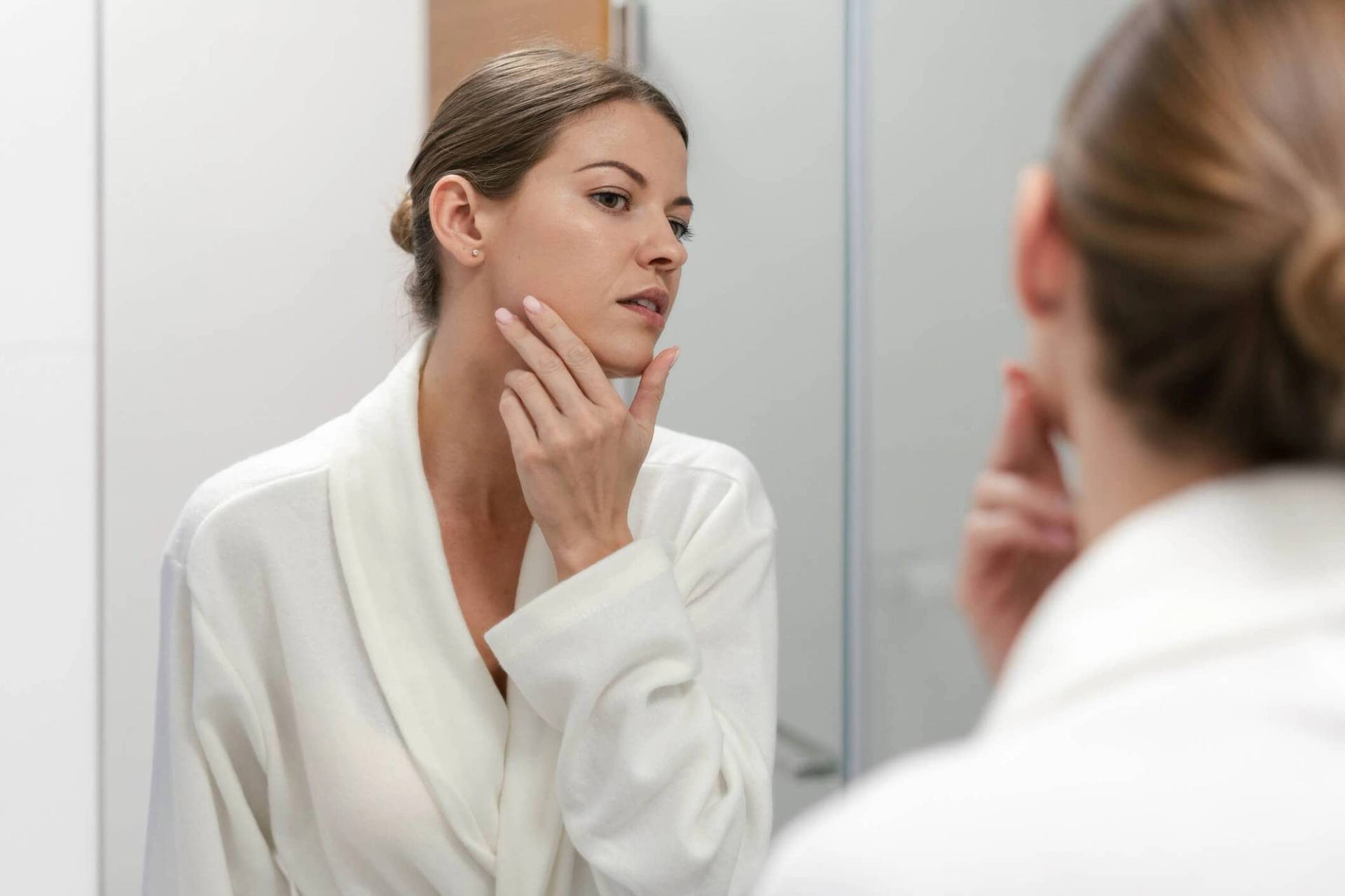 Femme examinant sa peau devant un miroir.