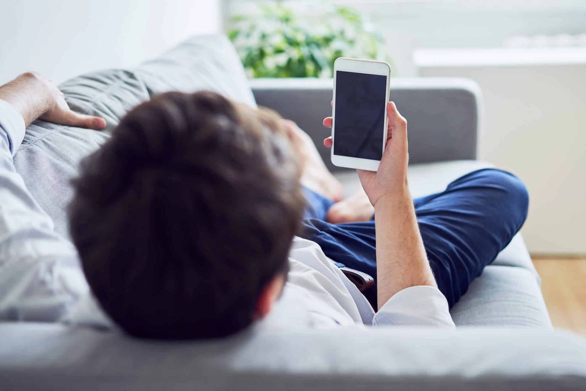 Homme allongé sur un canapé tenant un téléphone.