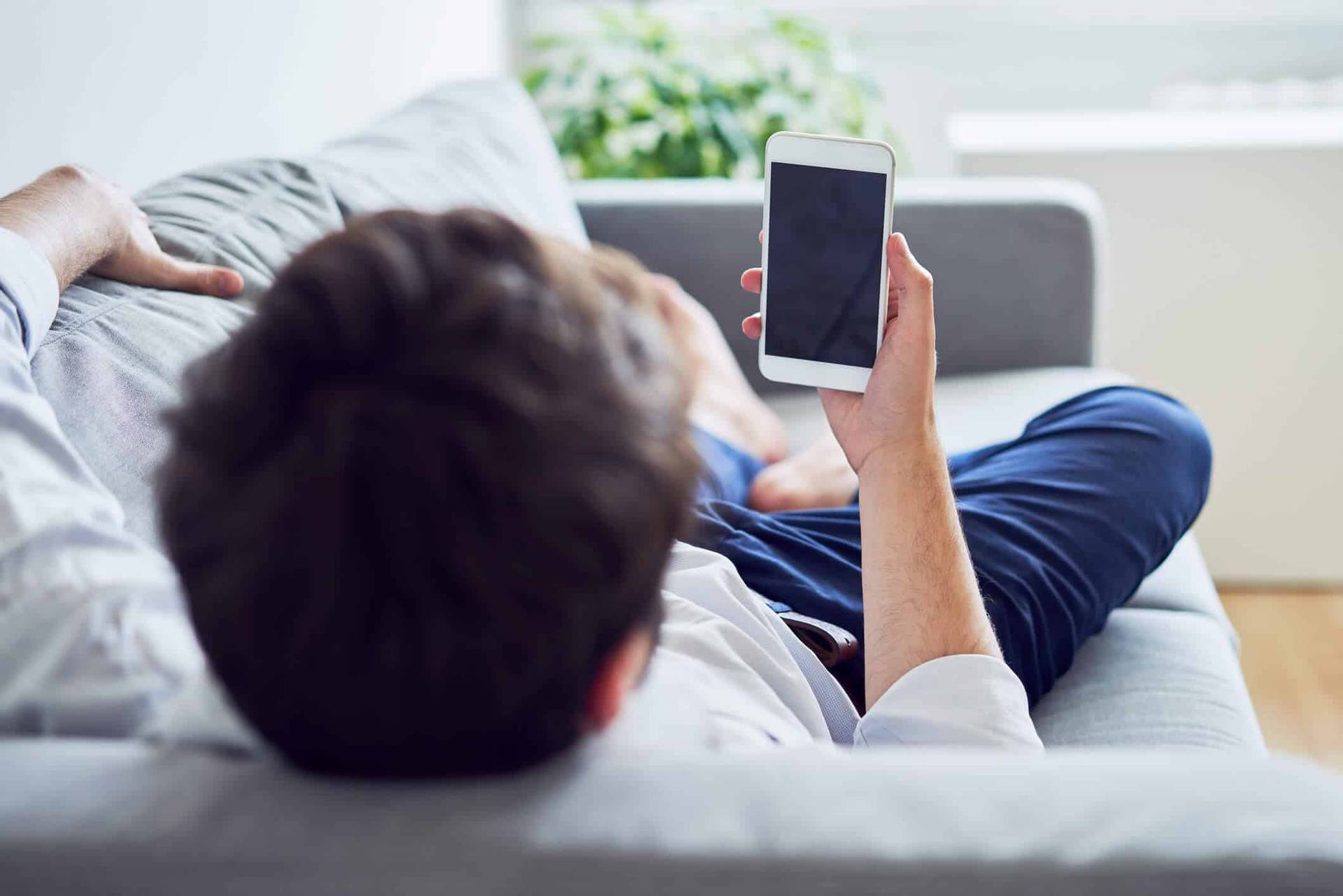 Homme allongé sur un canapé tenant un téléphone.
