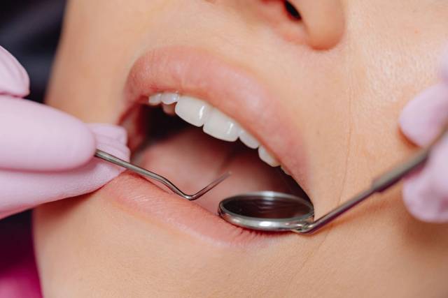 Examen de la bouche avec un miroir dentaire et des mains gantées.
