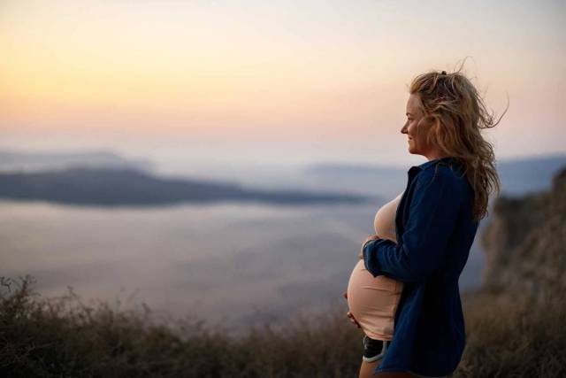 Femme au ventre arrondi photographiée à l’extérieur au coucher du soleil.