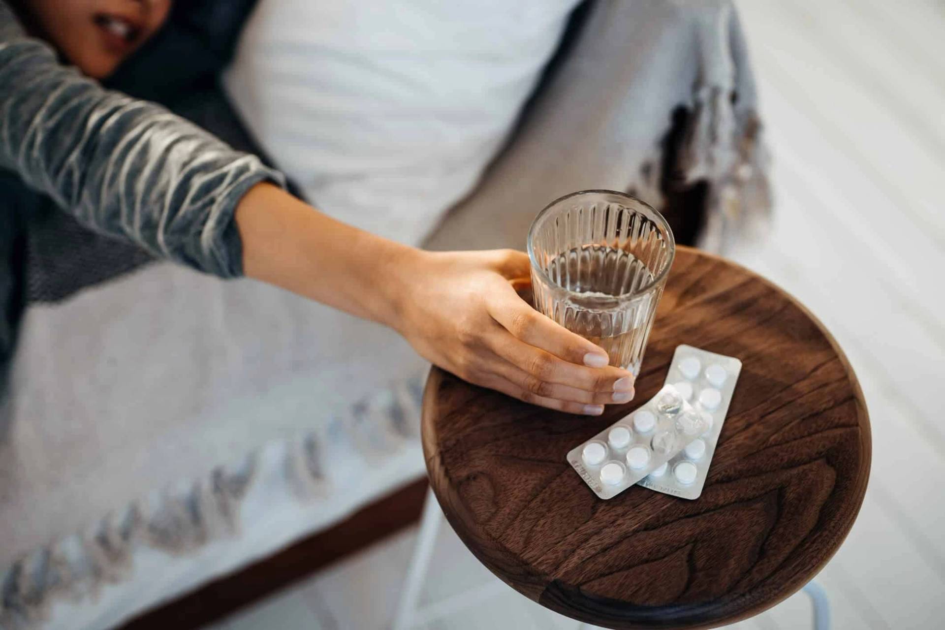 Main prenant un verre d’eau près d’une plaquette de comprimés.