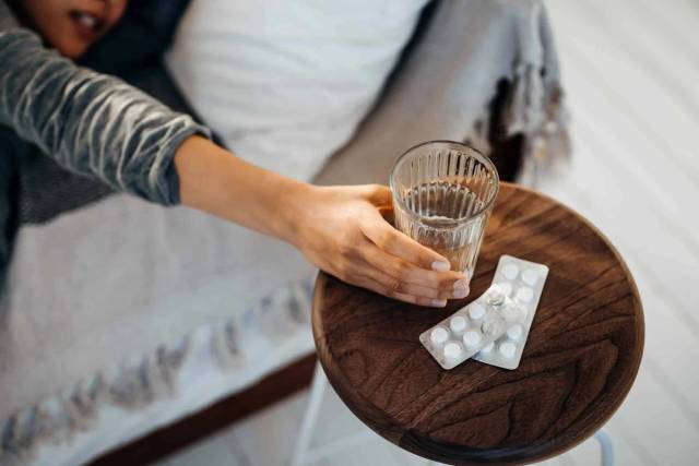 Main prenant un verre d’eau près d’une plaquette de comprimés.