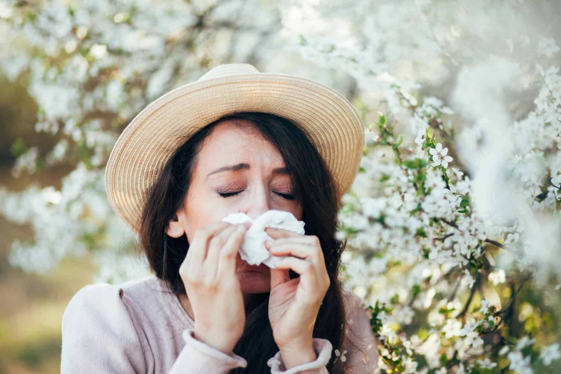 Femme portant un chapeau et se mouchant sous des fleurs.