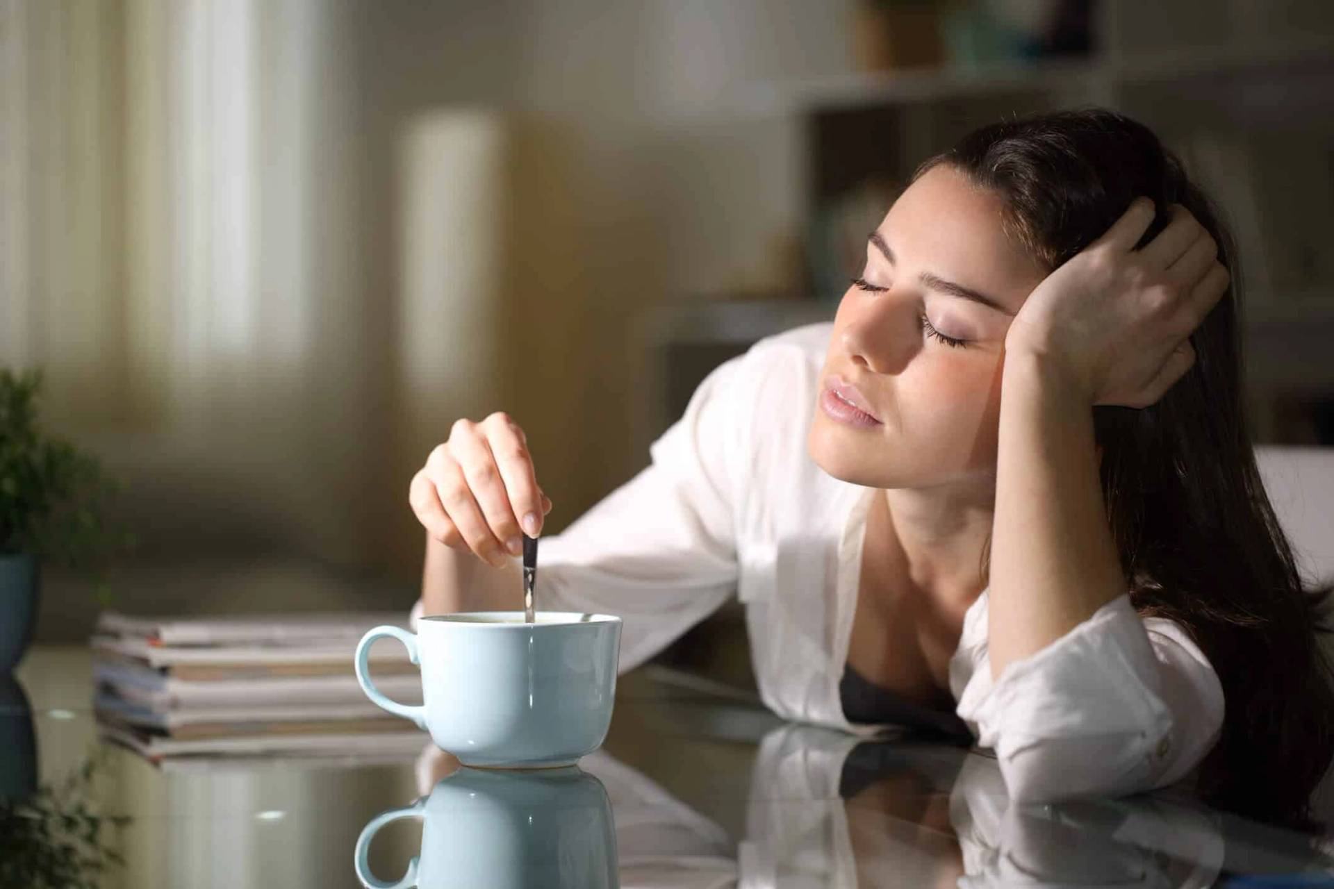 Femme appuyant la tête sur sa main devant une tasse.