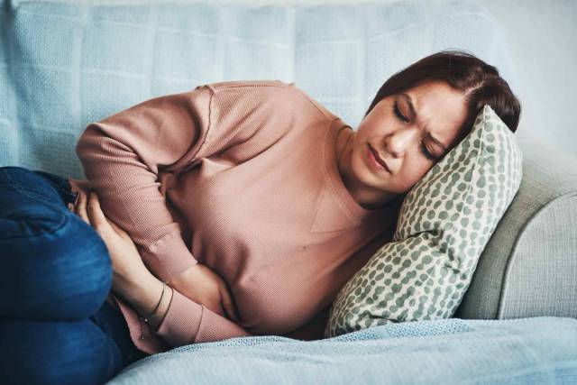 Femme recroquevillée sur un canapé, tenant son ventre.