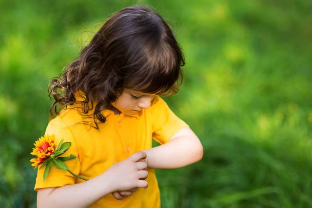 Enfant se grattant l’avant-bras à l’extérieur.