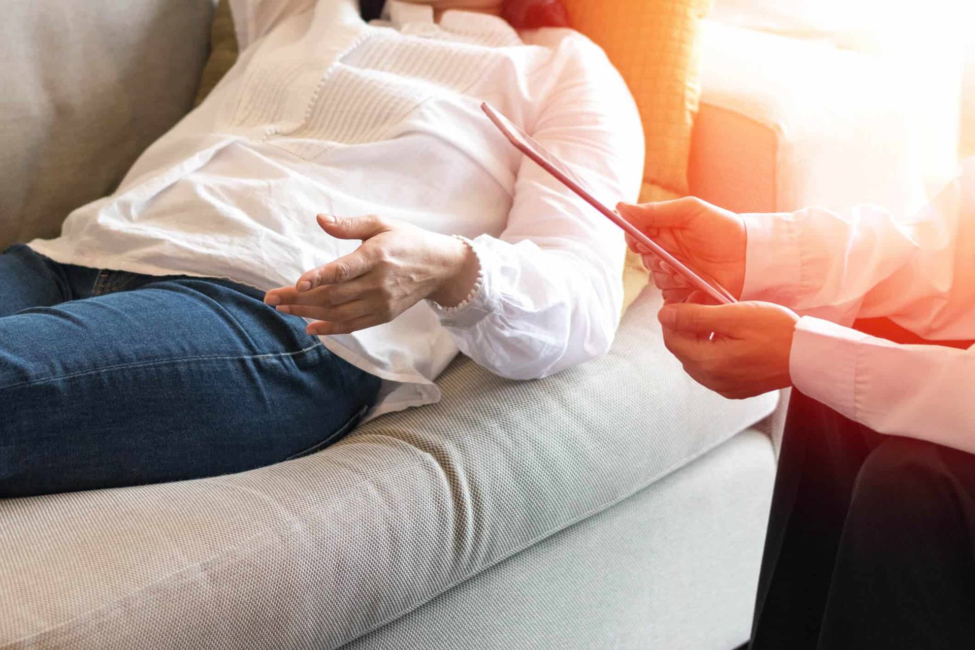 Personne allongée sur un divan, face à un interlocuteur tenant une tablette.