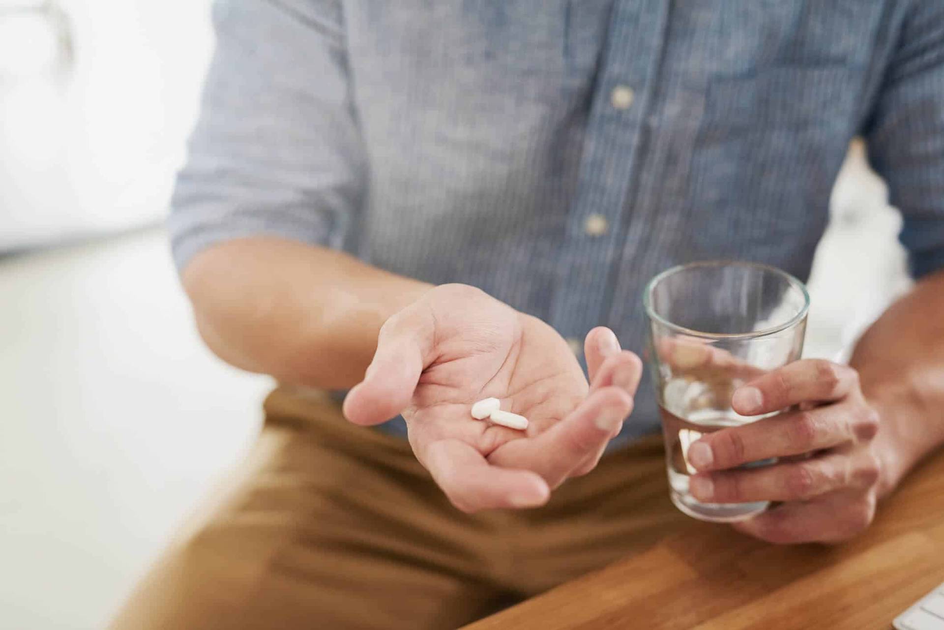 Personne tenant un comprimé et un verre d’eau.