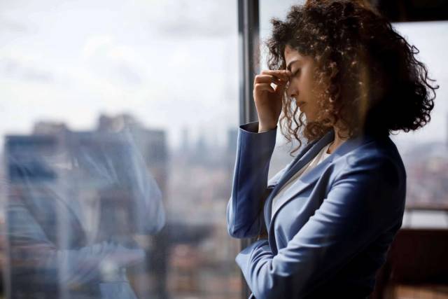 Femme devant une fenêtre, une main sur le haut du nez.