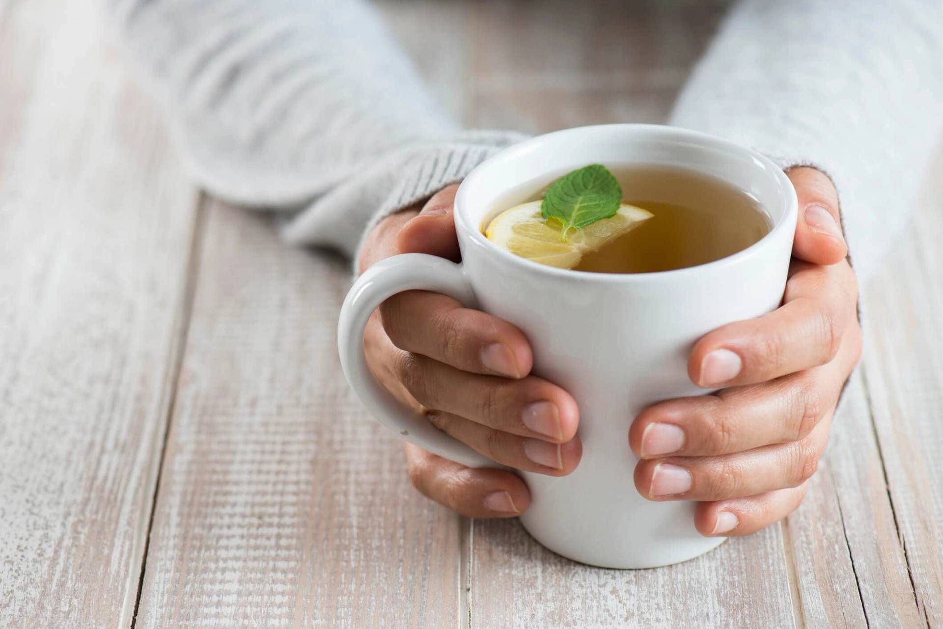 Mains tenant une tasse d’infusion au citron.