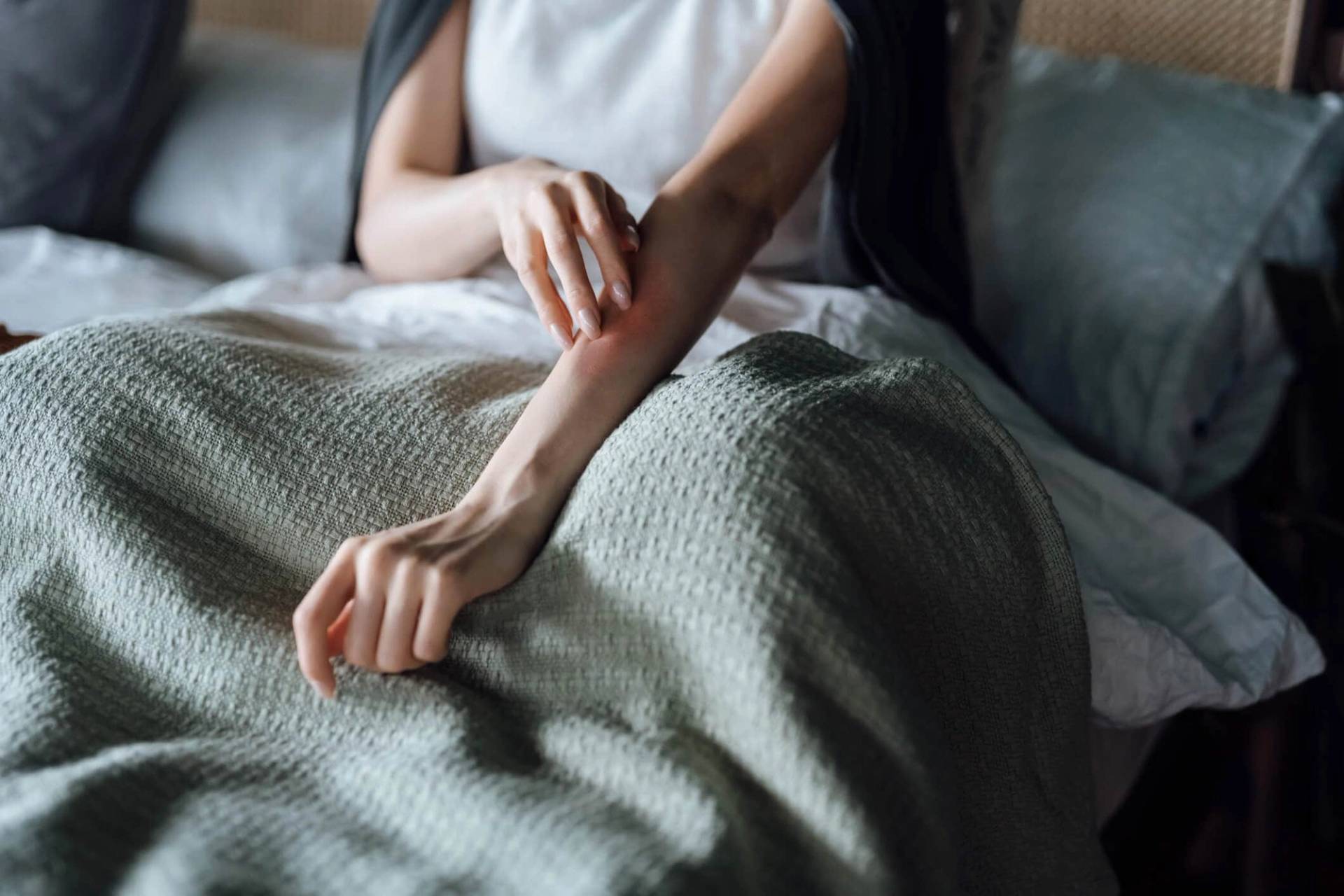 Personne assise sur un lit se grattant l’avant-bras.