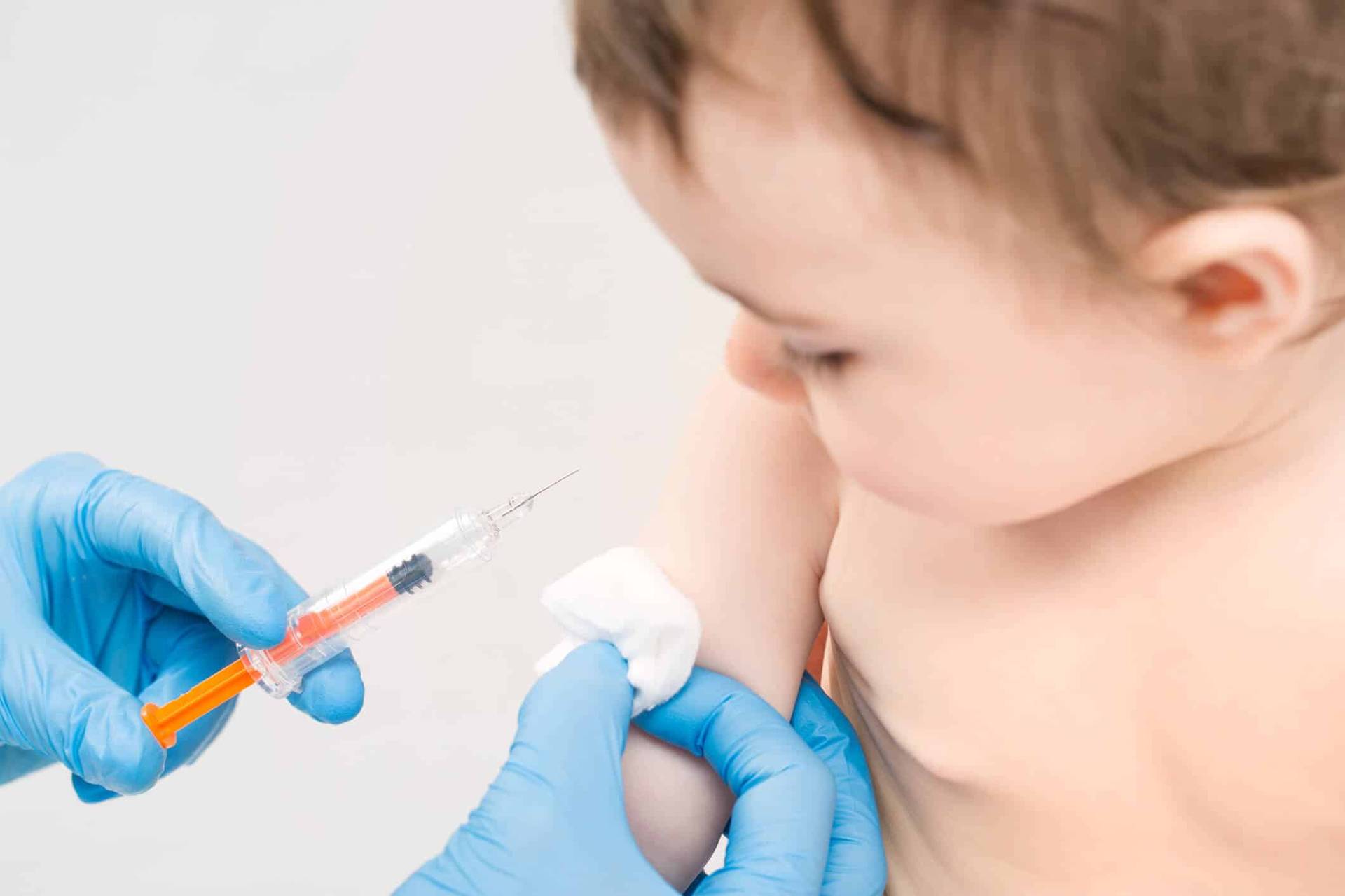 Personne gantée préparant une injection dans le bras d’un enfant.