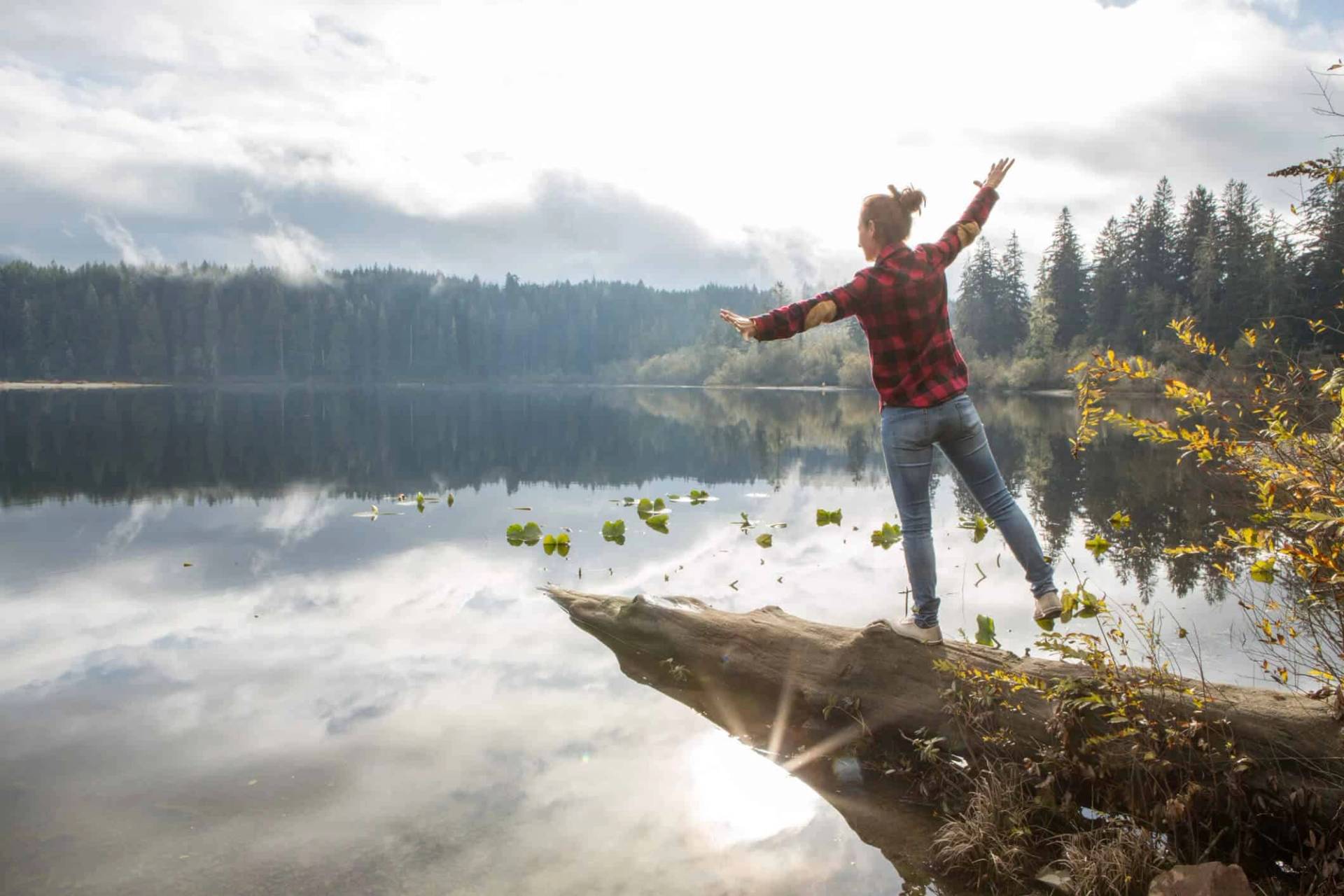 Personne debout, les bras écartés, au bord d’un lac.