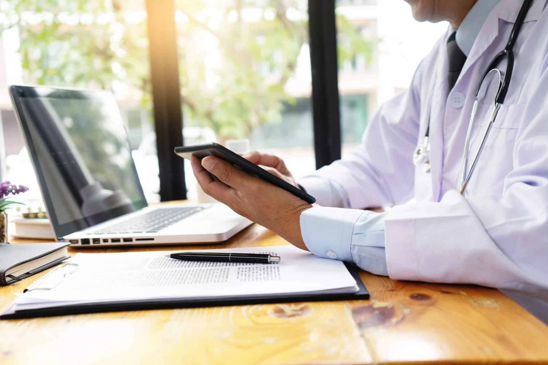 Personne en blouse blanche utilisant une tablette à un bureau.
