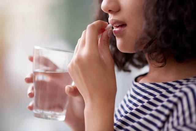 Femme prenant un comprimé avec un verre d’eau.