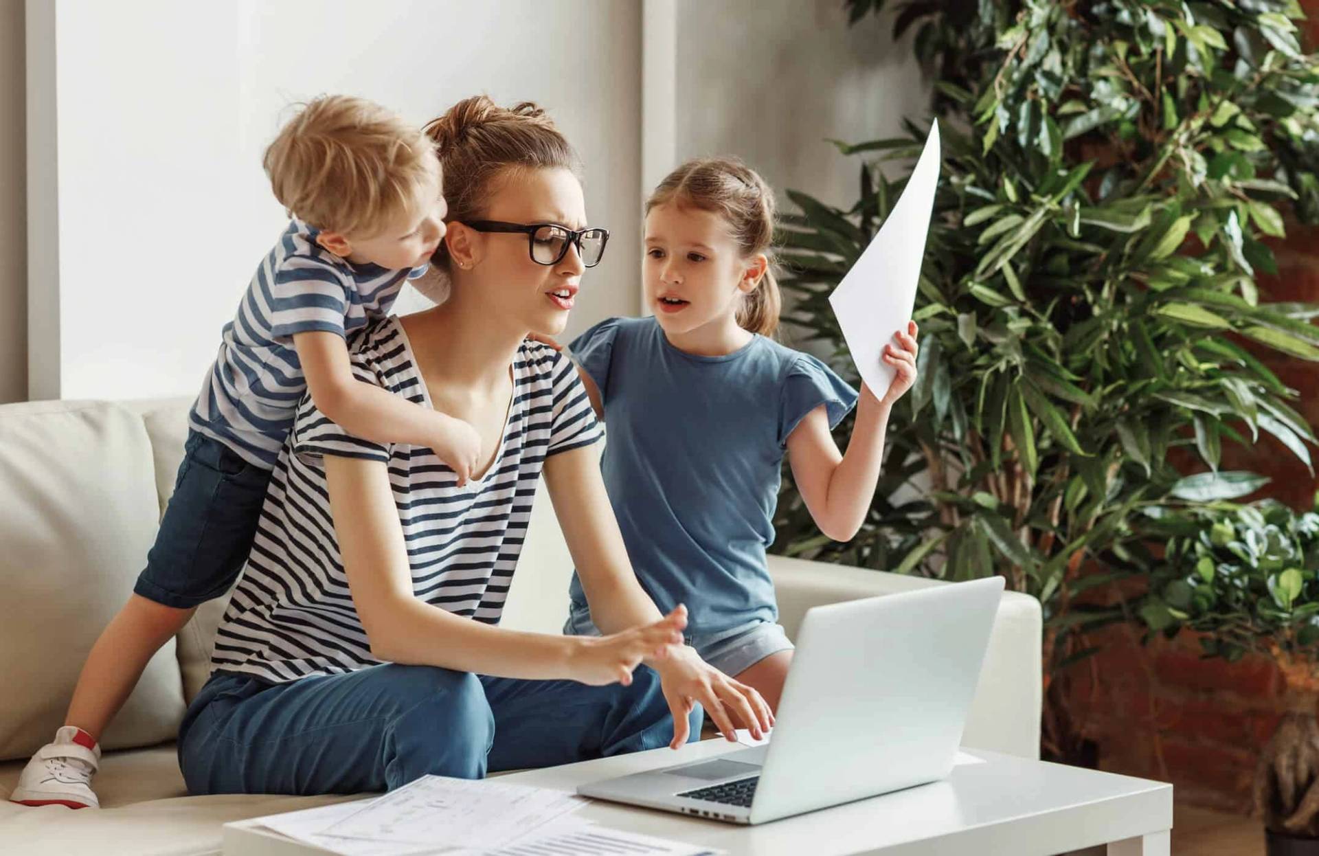 Adulte travaillant sur un ordinateur avec deux enfants à proximité.