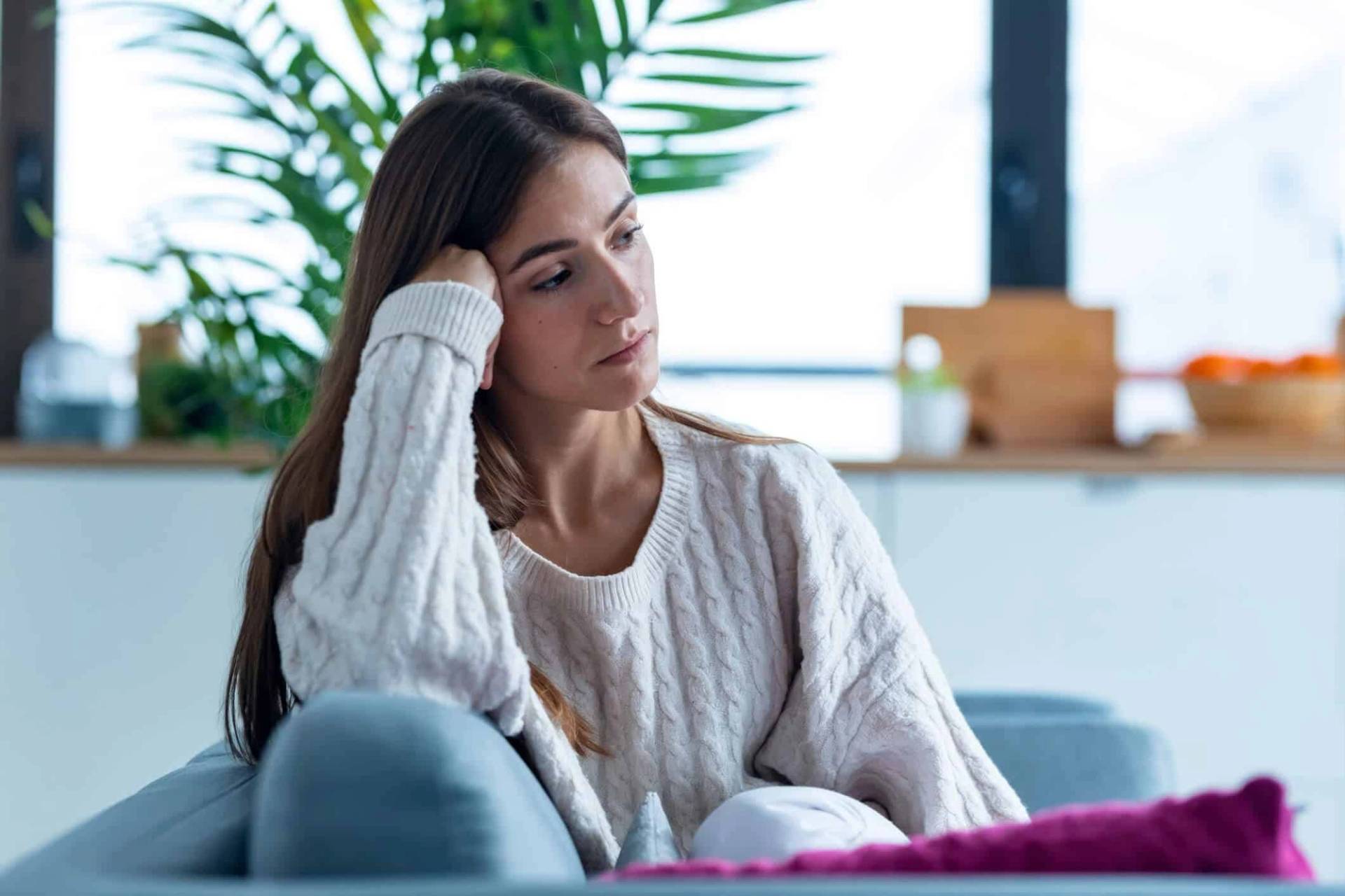 Femme assise sur un canapé, la tête appuyée sur une main.