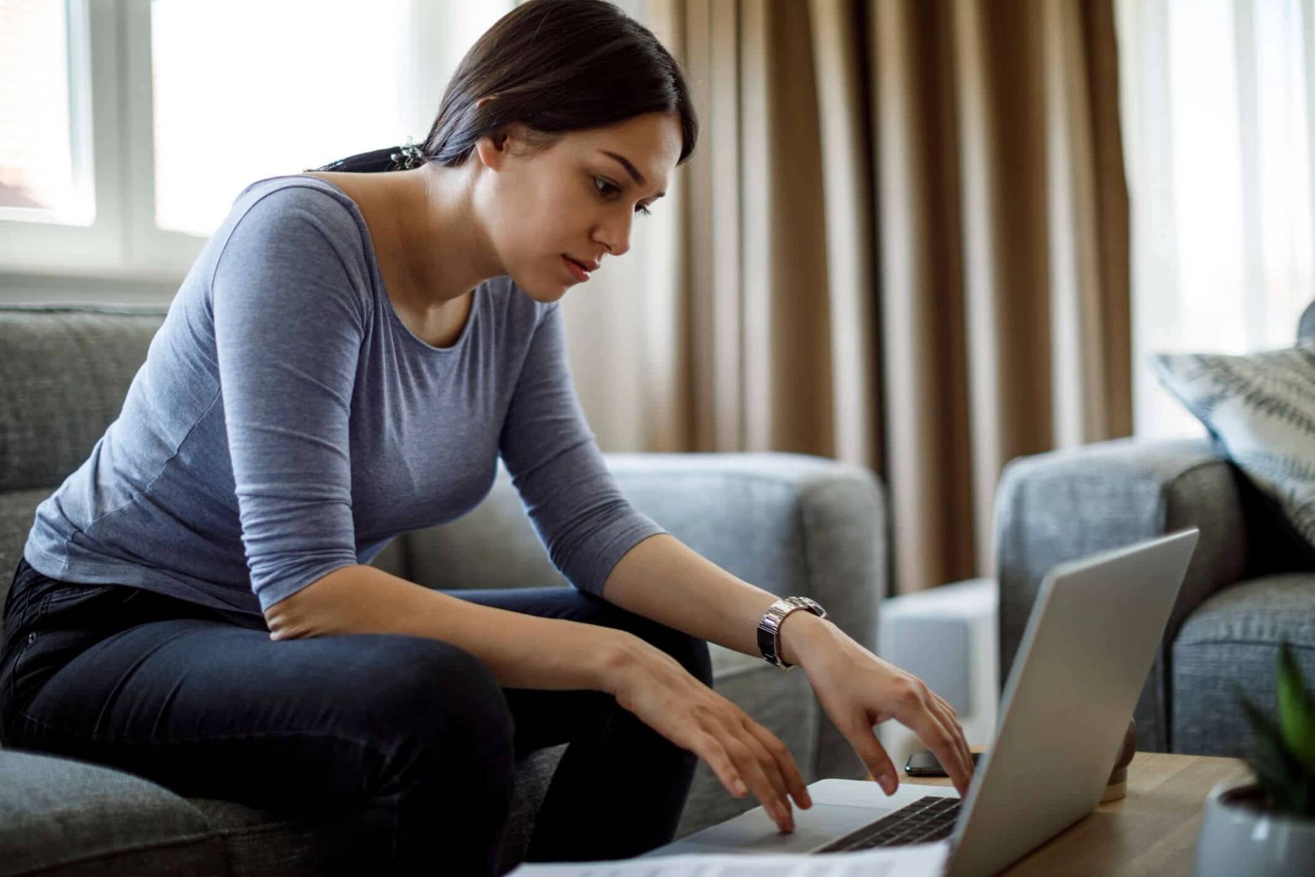 Femme assise sur un canapé devant son ordinateur portable.